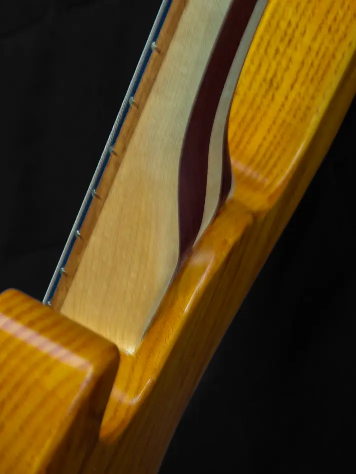 Close-up of the PE Bass neck pocket, showcasing the beautiful canary wood body and five-piece maple and mahogany neck. A detailed look at the precision craftsmanship and striking combination of woods.